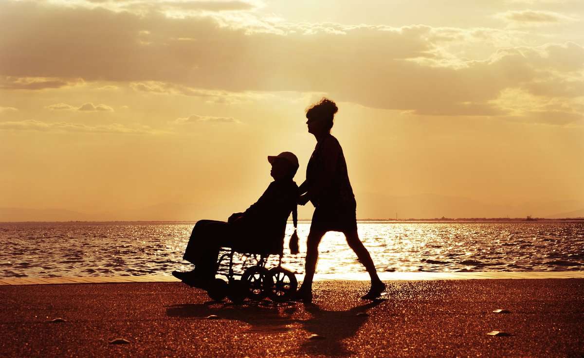 a man pushing a wheel chair next to the ocean.