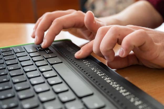 Blind man uses a computer keyboard with a braille display